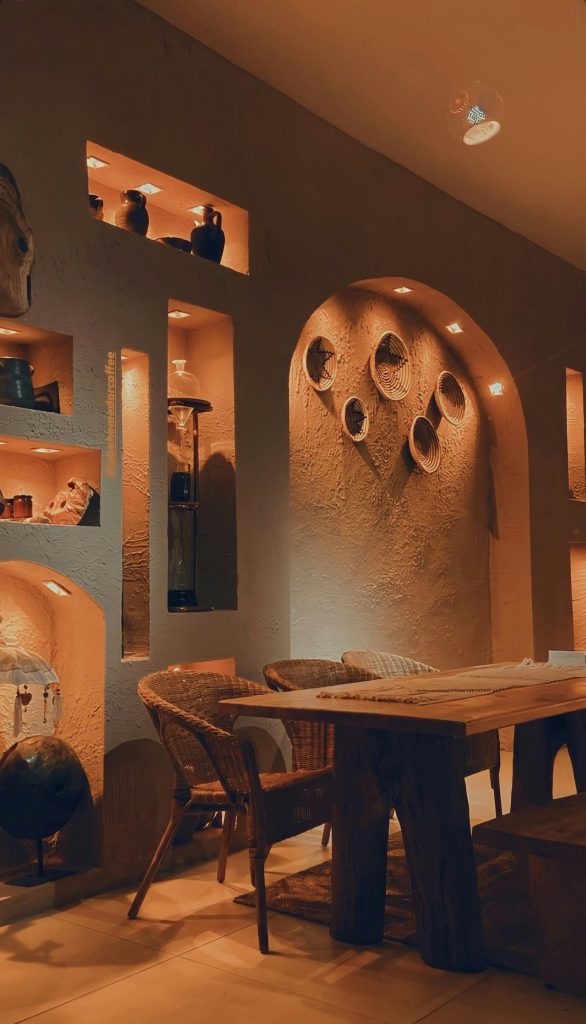 Cozy rustic living room featuring wooden table, chairs, and illuminated pottery display shelves.